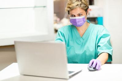 Masked clinician at laptop